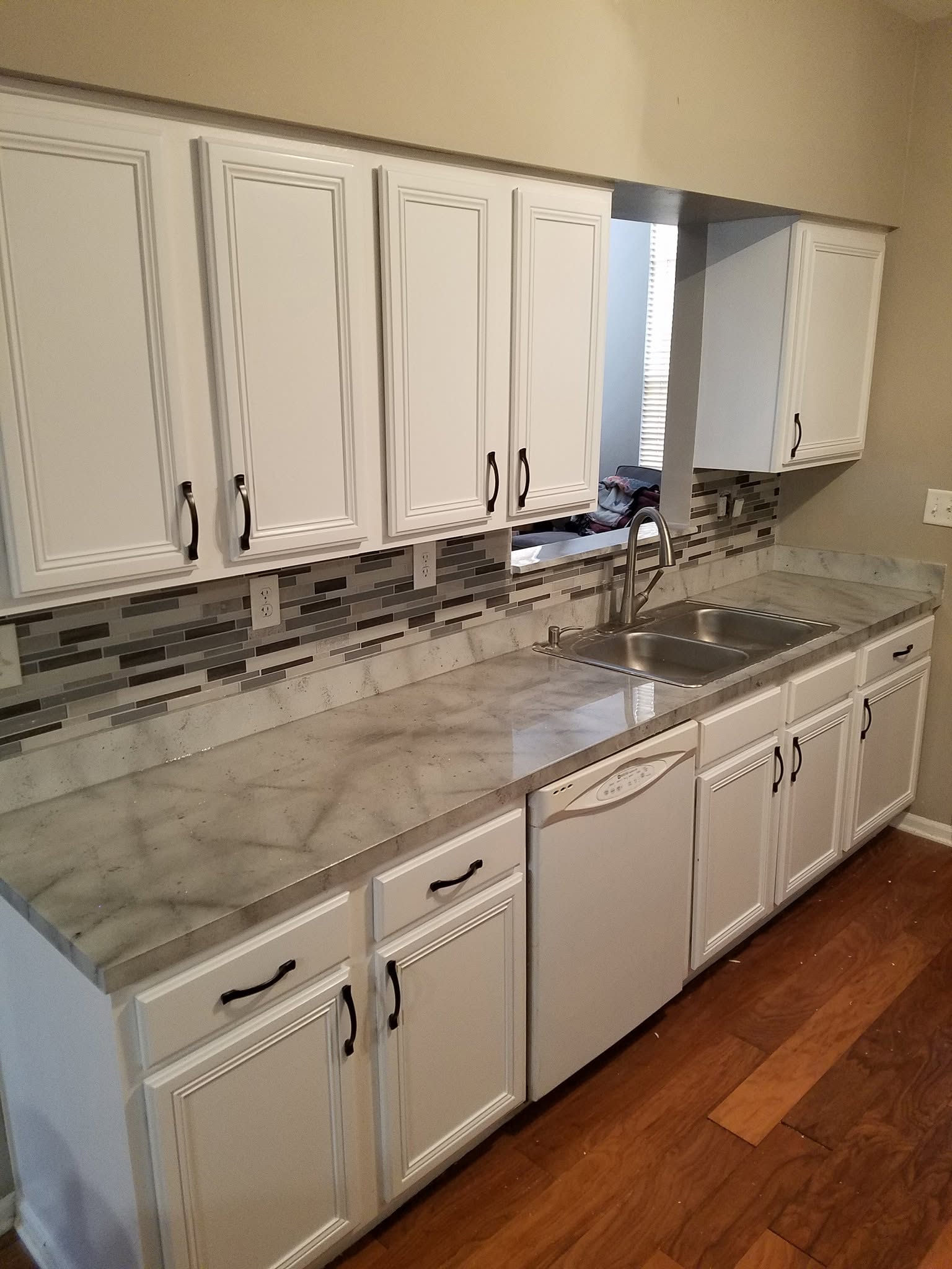 A freshly painted kitchen with refinished white cabinetry, a tile backsplash and new countertops.